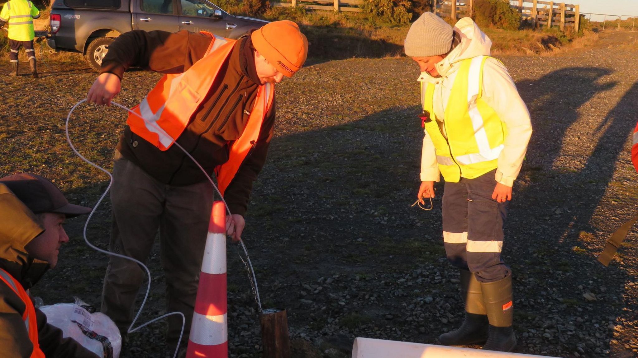 Dr Ema Frery (right) in a high-visibility with a colleague looking down at some test equipment 