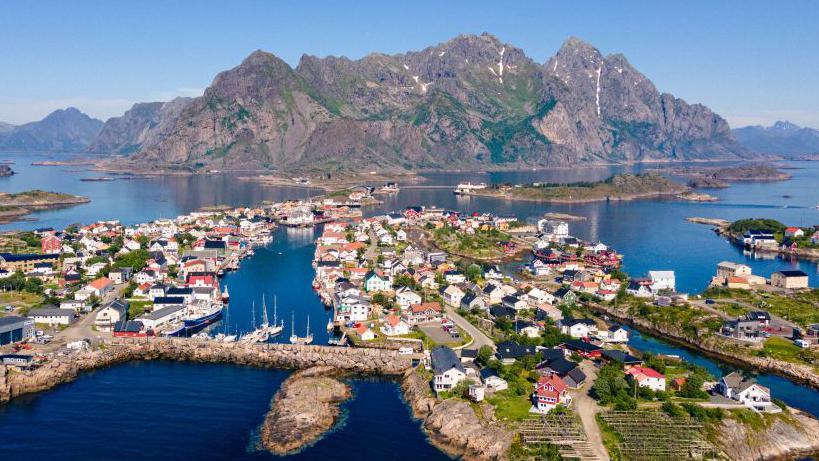 Aerial view of the village of Hennigsvaer in northern Norway. Houses on islands are in the foreground with a large mountain in the background.