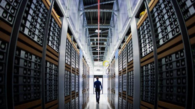 A man walks between racks of servers in a data centre.