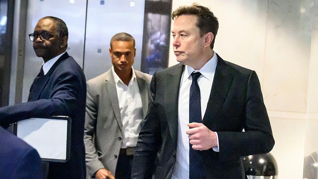 Musk appears walking into the courthouse wearing a black suit and tie with a white shirt