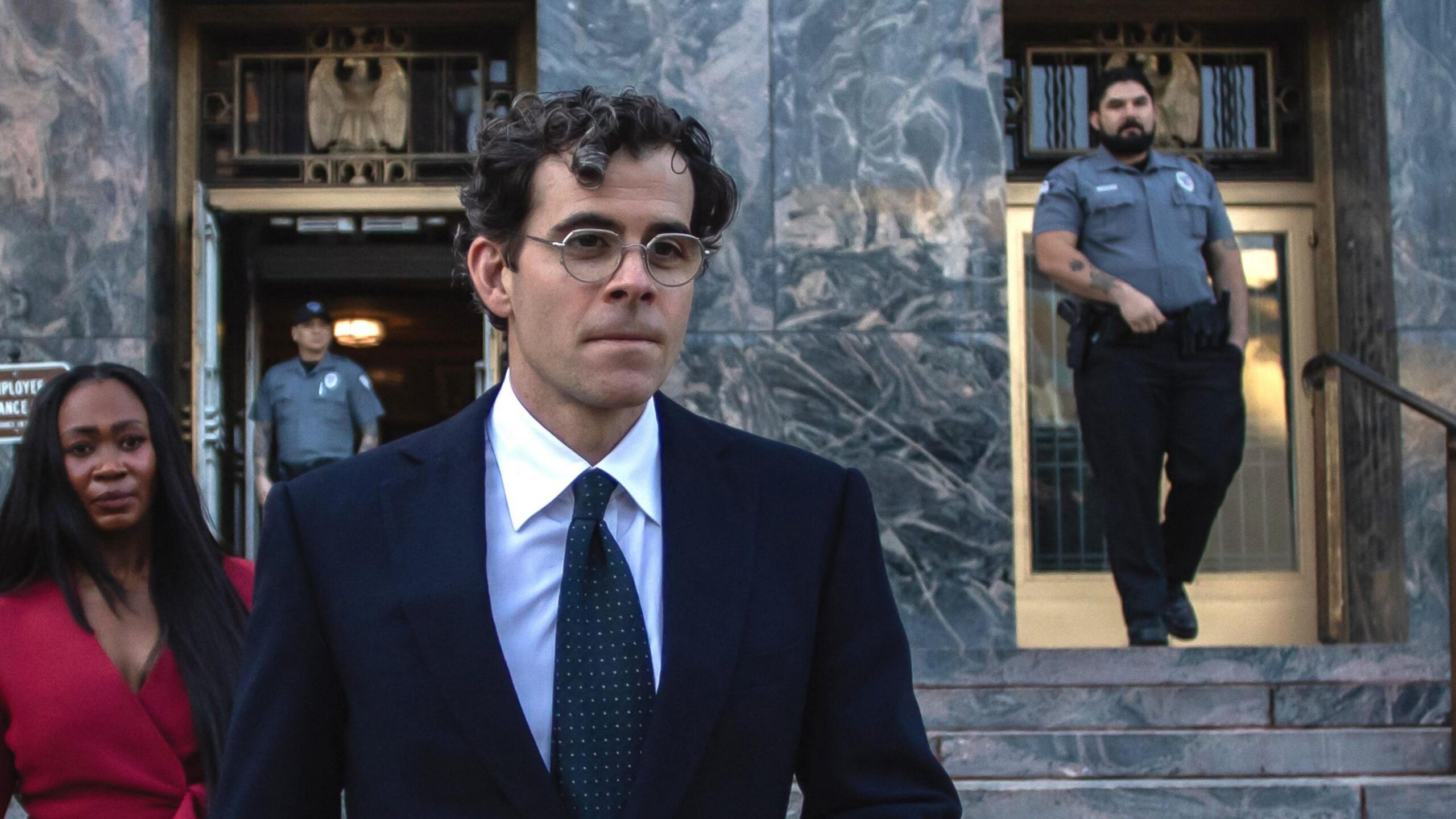 Adam Mosseri, with dark curly hair and glasses, in a dark suit, white shirt, and spotted tie, seen against the marble-façade and steps of the Los Angeles County Superior Court.  